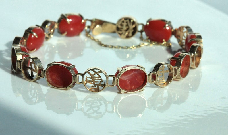 May include: A gold bracelet with red coral stones and Chinese characters. The bracelet is made of 14k gold and features a delicate chain.