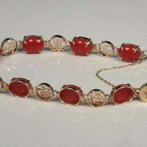 May include: A gold bracelet with red coral stones and Chinese characters. The bracelet has a clasp with a small chain.
