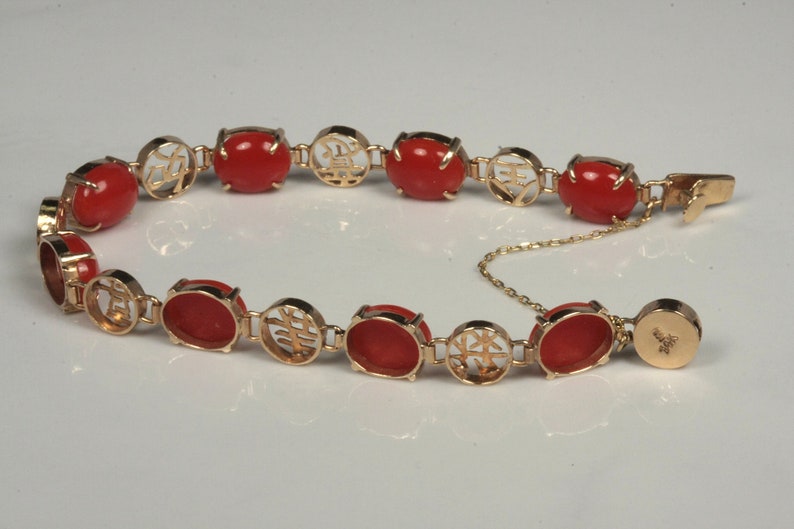 May include: A gold bracelet with red coral stones and Chinese characters. The bracelet has a clasp with a small chain.