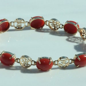 May include: A gold bracelet with red coral stones and Chinese characters. The bracelet has a clasp.