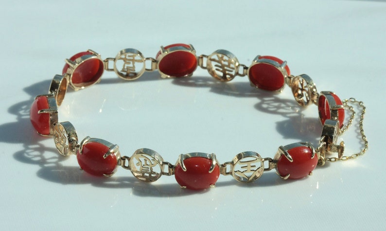 May include: A gold bracelet with red coral stones and Chinese characters. The bracelet has a clasp.