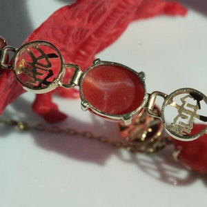 May include: A red coral bracelet with gold accents. The gold accents feature Chinese characters.