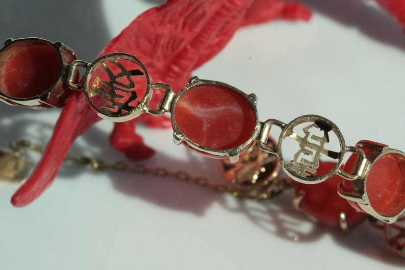 May include: A red coral bracelet with gold accents. The gold accents feature Chinese characters.