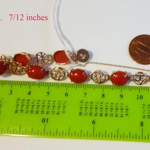 May include: A red coral bracelet with gold accents and a clasp. The bracelet is 7/12 inches long and weighs 10.7 grams. The bracelet is measured on a ruler.