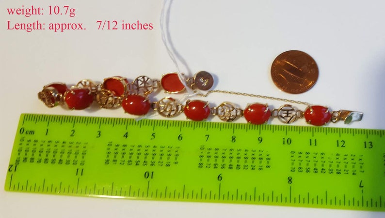 May include: A red coral bracelet with gold accents and a clasp. The bracelet is 7/12 inches long and weighs 10.7 grams. The bracelet is measured on a ruler.