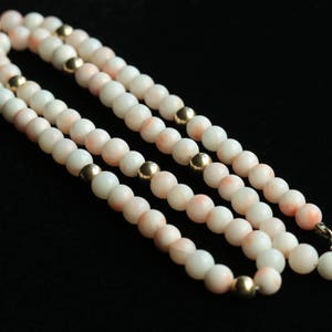 May include: A multi-strand necklace made of white and pink coral beads with gold accents.