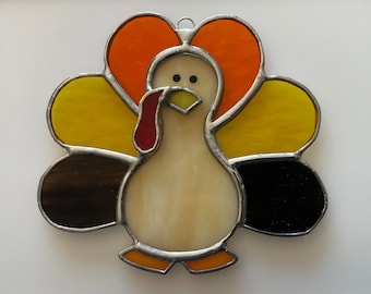 May include: A stained glass turkey ornament with a white body, orange and yellow feathers, and black tail feathers.