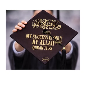 May include: A brown graduation cap with gold lettering and a black tassel. The cap features Arabic script and the English text "MY SUCCESS IS ONLY BY ALLAH QURAN 11:88". The cap is held up by a person.