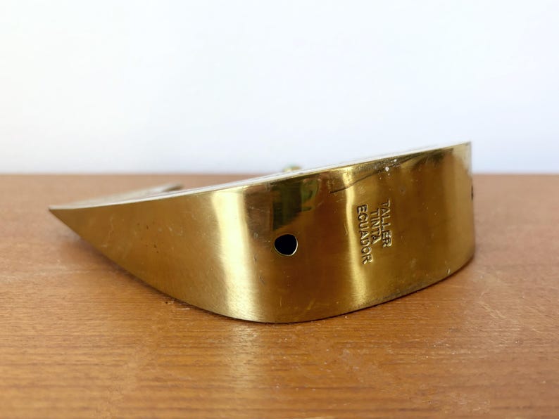 May include: A gold-colored metal paperweight shaped like a boat with the text "Taller Tinta Ecuador" engraved on the side.