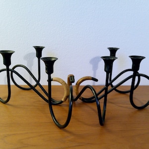 May include: Black metal candelabra with five candle holders. The design features looping, curved arms and a woven detail in the center. A decorative piece for a table or mantel.
