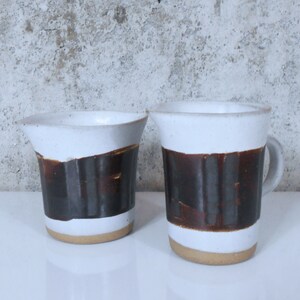 Pode incluir: Duas canecas de cerâmica com listras marrons e brancas. A caneca à direita tem uma alça.