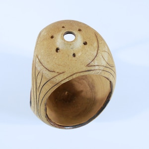 May include: A small, brown ceramic pot with a hole in the top and a decorative design around the rim. The pot has a smooth, rounded shape and is perfect for planting small plants or herbs.