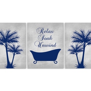 May include: A three-panel wall art set with a spa theme. Each panel features a light gray background with dark blue palm trees and a bathtub silhouette. The center panel has the words "Relax Soak Unwind".