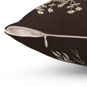 May include: A decorative throw pillow with a dark brown background and a floral design. The pillow features a zipper closure and a cream-colored interior. The floral pattern includes light green leaves and small, peach-colored flowers.