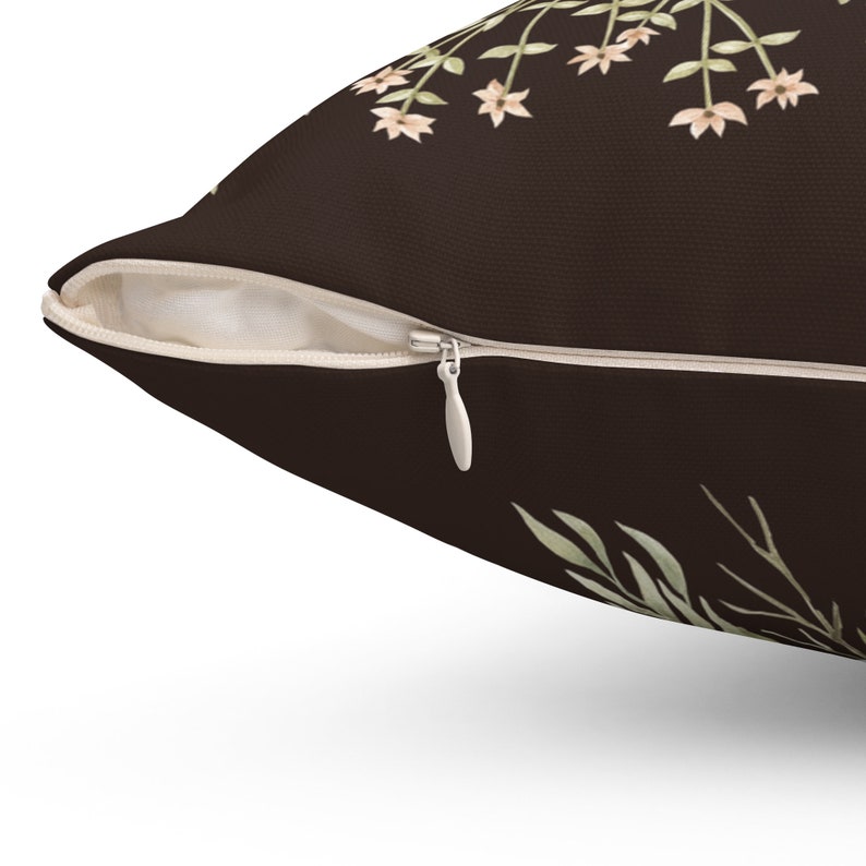 May include: A decorative throw pillow with a dark brown background and a floral design. The pillow features a zipper closure and a cream-colored interior. The floral pattern includes light green leaves and small, peach-colored flowers.