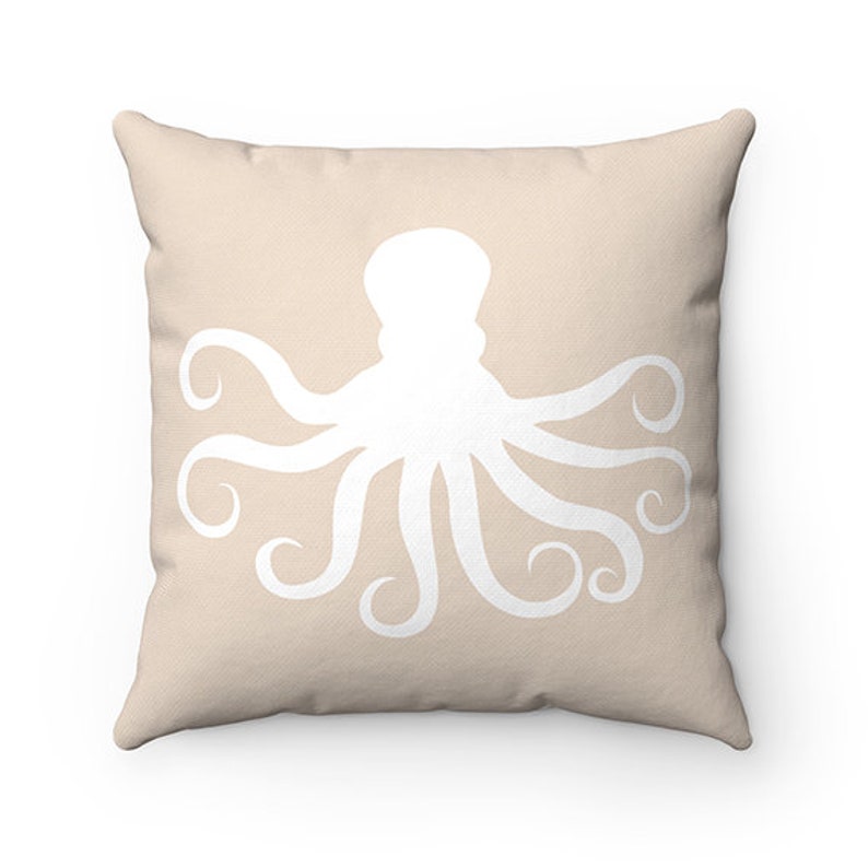 May include: A beige throw pillow with a white silhouette of an octopus. The octopus has eight tentacles and is centered on the pillow.
