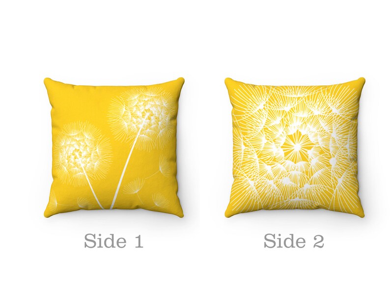 May include: Two-sided yellow throw pillow with a white dandelion design. One side features a single dandelion with seeds blowing in the wind, while the other side features a cluster of dandelions.