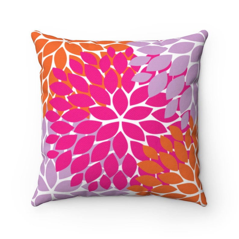 Puede incluir: Una almohada cuadrada con un patr&oacute;n floral en tonos rosa, naranja y morado. La almohada tiene un fondo blanco y presenta un patr&oacute;n repetitivo de p&eacute;talos de flores estilizados.