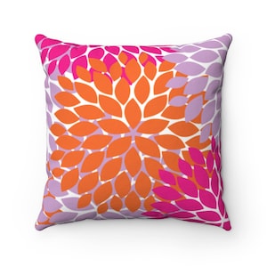 Puede incluir: Una almohada cuadrada con un patr&oacute;n floral. La almohada presenta un fondo blanco con formas de flores superpuestas de color naranja, rosa y morado.