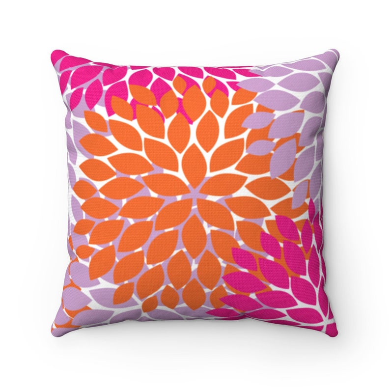 Puede incluir: Una almohada cuadrada con un patr&oacute;n floral. La almohada presenta un fondo blanco con formas de flores superpuestas de color naranja, rosa y morado.