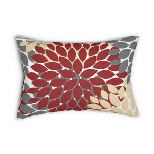 May include: A rectangular throw pillow with a floral pattern in shades of red, gray, and beige. The pillow features a repeating pattern of stylized flower petals.