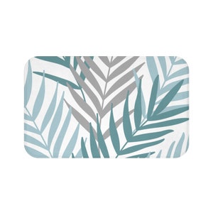 May include: A white bath mat with a pattern of teal and gray palm leaves.