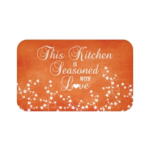 May include: Orange kitchen mat with white vines and the text "This Kitchen is Seasoned with Love" in a white cursive font.