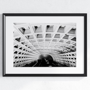 May include: Black and white photograph of a tunnel interior. The ceiling is a repeating pattern of square and rectangular shapes. The tunnel curves into the distance, with a dark area at the end. The image is framed in a black frame.