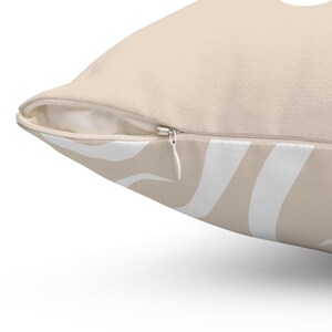 May include: A beige throw pillow with a white abstract pattern. The pillow has a zipper closure.