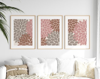 Puede incluir: Tres impresiones artísticas florales enmarcadas. Cada impresión presenta un diseño floral estilizado en tonos de rosa, marrón y gris sobre un fondo crema. Los marcos son de color madera clara y la obra de arte se exhibe sobre un sofá blanco.