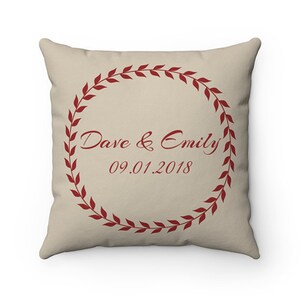 May include: A beige throw pillow with a red wreath design. The wreath has leaves and the text "Dave & Emily 09.01.2018" in the centre.