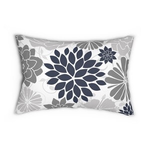 May include: Rectangular decorative pillow with a floral pattern in shades of gray and navy blue. The pillow features large stylized flowers and smaller floral accents on a white background. A stylish home decor item.