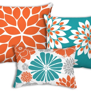 May include: Three decorative throw pillows with floral patterns. The pillows are in shades of orange, teal, white, and gray.