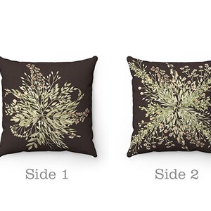 May include: Two square throw pillows with a dark brown background. Each pillow features a symmetrical floral design in shades of green and beige. The text "Side 1" and "Side 2" are below the pillows.