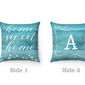 May include: Two-sided decorative pillow with a turquoise blue background. One side features the text "home sweet home" in white script. The other side features a white letter "A" in a white frame with a floral design.