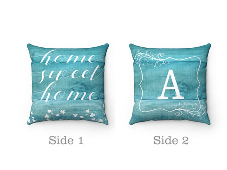 May include: Two-sided decorative pillow with a turquoise blue background. One side features the text "home sweet home" in white script. The other side features a white letter "A" in a white frame with a floral design.