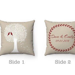 May include: A two-sided cushion with a beige background. One side features a white silhouette of a tree with two red birds. The other side has a red wreath with the text "Dave & Emily 09.01.2018".