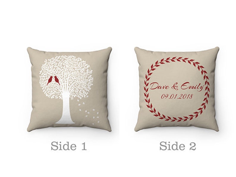 May include: A two-sided cushion with a beige background. One side features a white silhouette of a tree with two red birds. The other side has a red wreath with the text "Dave & Emily 09.01.2018".