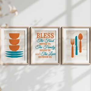 May include: Three framed prints with a rustic wood background. The center print features the text "BLESS The Food BEFORE US, The Family BESIDE US, and The Love BETWEEN US." The left print shows a stack of orange bowls and blue plates. The right print shows a fork, knife, and spoon.