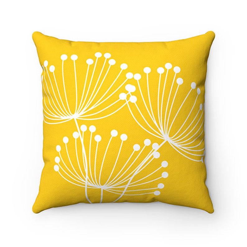 May include: A yellow throw pillow with a white floral design. The pillow features a stylized floral pattern with white stems and circles on a bright yellow background.