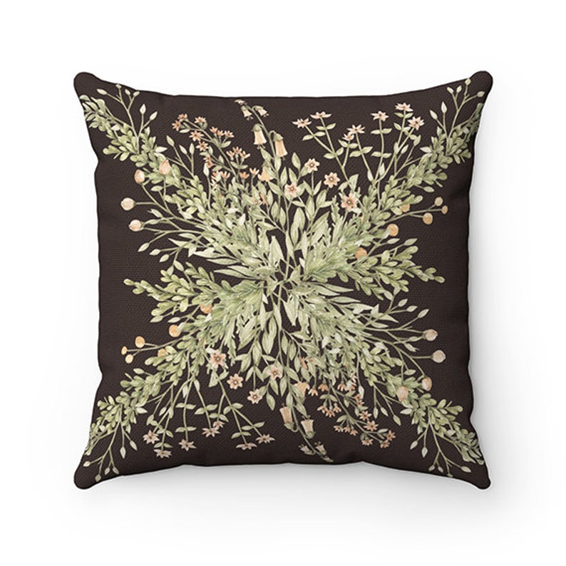 May include: Square throw pillow with a dark brown background and a floral design. The design features light green leaves, small beige flowers, and beige berries arranged in a symmetrical pattern.