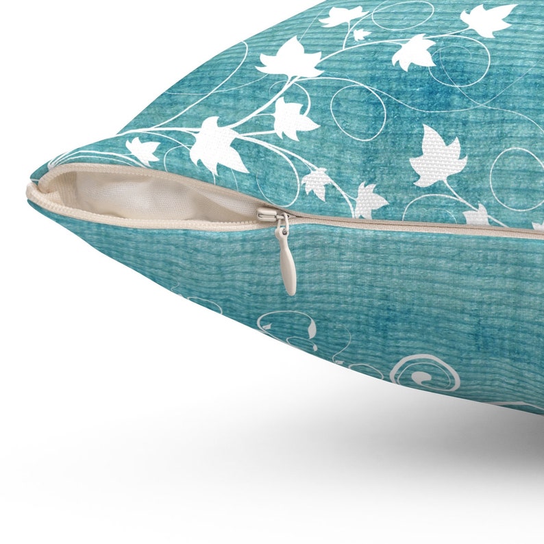 May include: A teal blue throw pillow with a white floral pattern and a zipper closure.