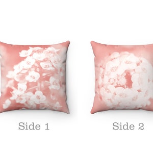 May include: Two square throw pillows with a floral design. The pillows have a soft coral background with a white floral pattern. The text "Side 1" and "Side 2" are printed below the pillows.