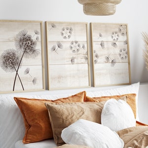 May include: Three framed prints with a woodgrain background and black line drawings of dandelions. The prints are hung above a bed with white and brown pillows.