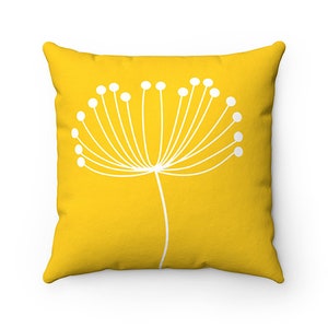 May include: A yellow throw pillow with a white stylized flower design. The flower has a long stem and many small white circles at the end of each branch.