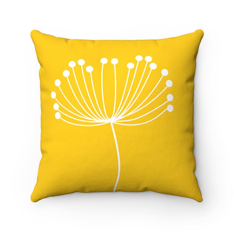 May include: A yellow throw pillow with a white stylized flower design. The flower has a long stem and many small white circles at the end of each branch.