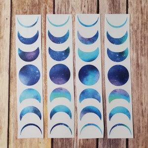 May include: Four white sheets of paper with blue and purple galaxy moon phase stickers. Each sheet has a different moon phase design.