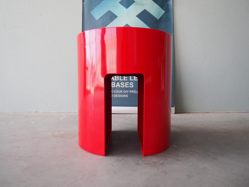 May include: A vibrant red, cylindrical stool with a rectangular cutout. The glossy finish reflects light, highlighting its smooth surface. The stool's design is modern and minimalist, suitable for various interior settings.