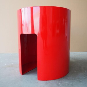 May include: A vibrant red, cylindrical side table with a glossy finish. The modern design features a cutout section, creating a unique visual element. The table is approximately 24 inches tall and 18 inches in diameter.