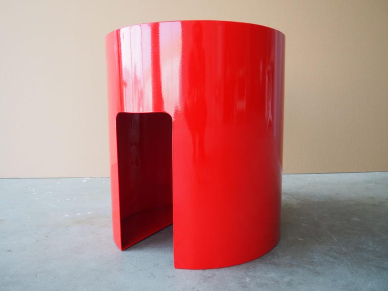 May include: A vibrant red, cylindrical side table with a glossy finish. The modern design features a cutout section, creating a unique visual element. The table is approximately 24 inches tall and 18 inches in diameter.